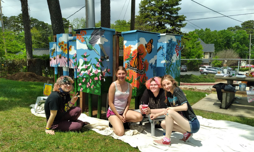 Students painting utilities boxes with flowers and butterflies