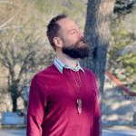 Man under tree shade wearing maroon sweater