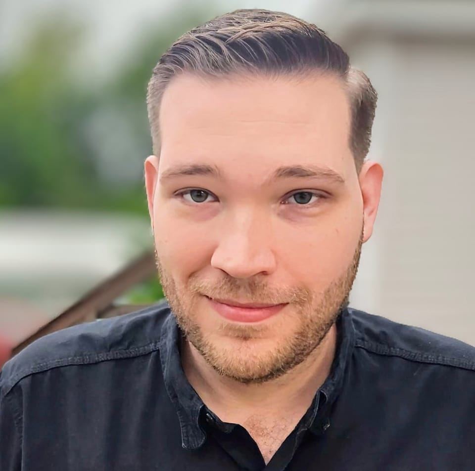 White man in black dress shirt with blurred trees in the background