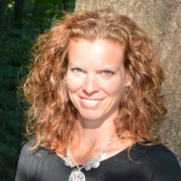 Woman with red hair standing in front of a tree smiling