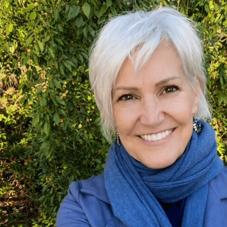 smiling woman with short gray hair with leafy wall in the background