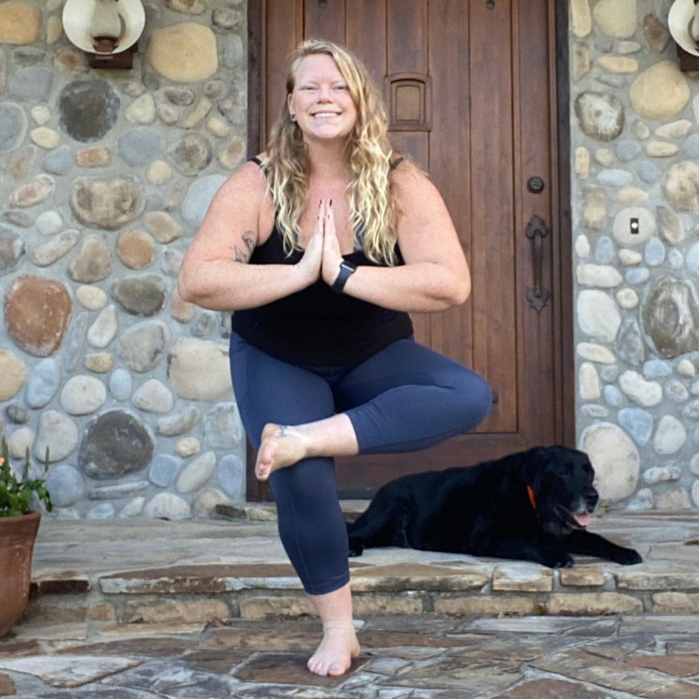 Young woman standing in front of stone building in a yoga pose